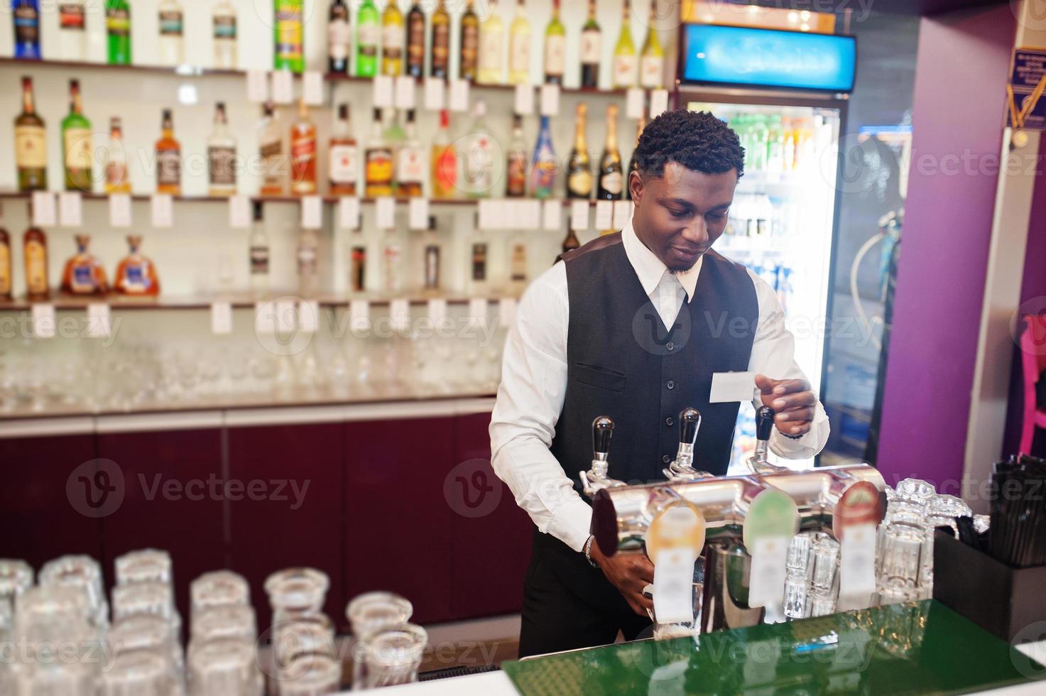 barman afro-américain au bar versant de la bière fraîche du robinet dans le verre du pub. photo