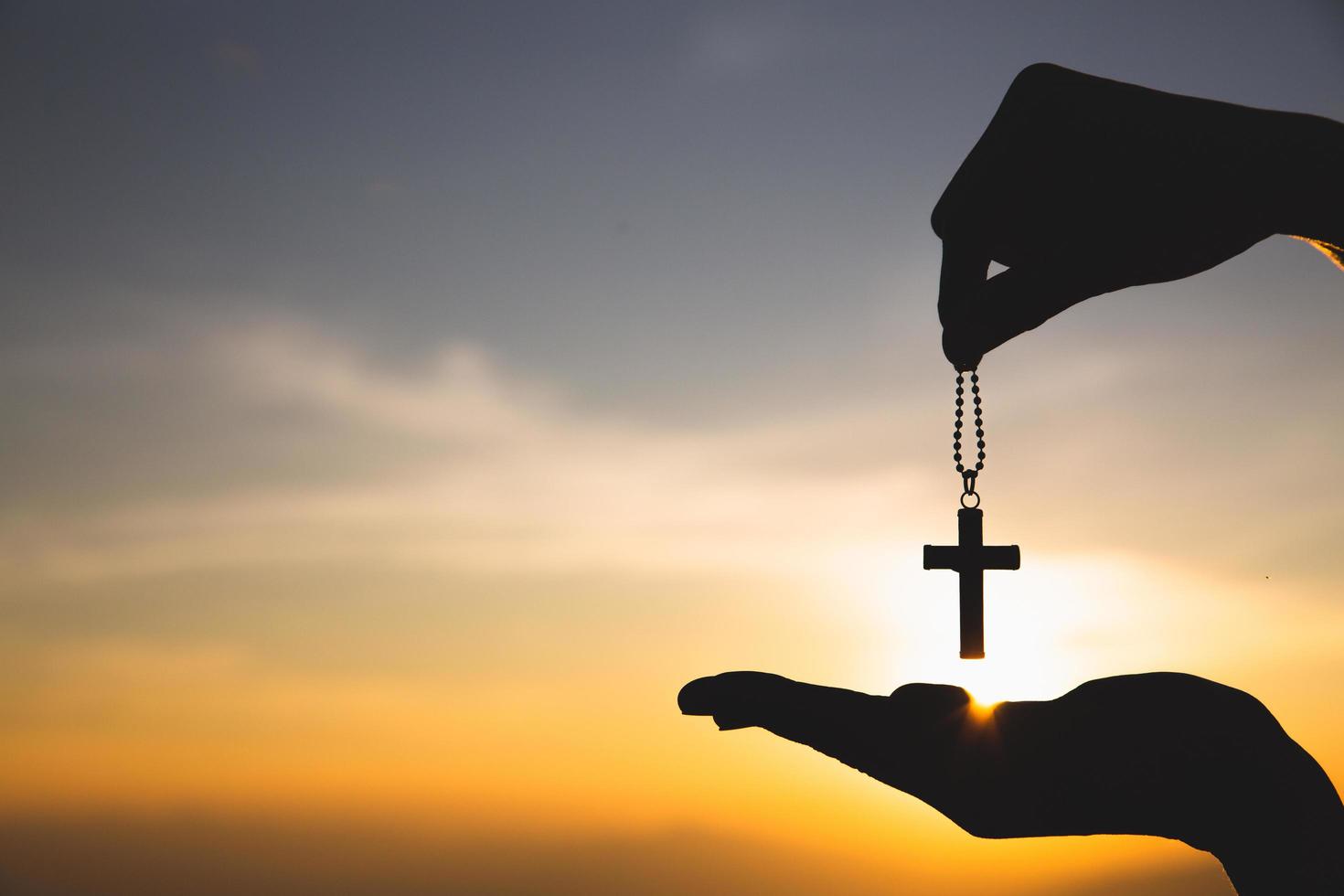 silhouette de main tenant collier crucifix fond lever du soleil. concept pour chrétien, christianisme, religion catholique, dieu. photo