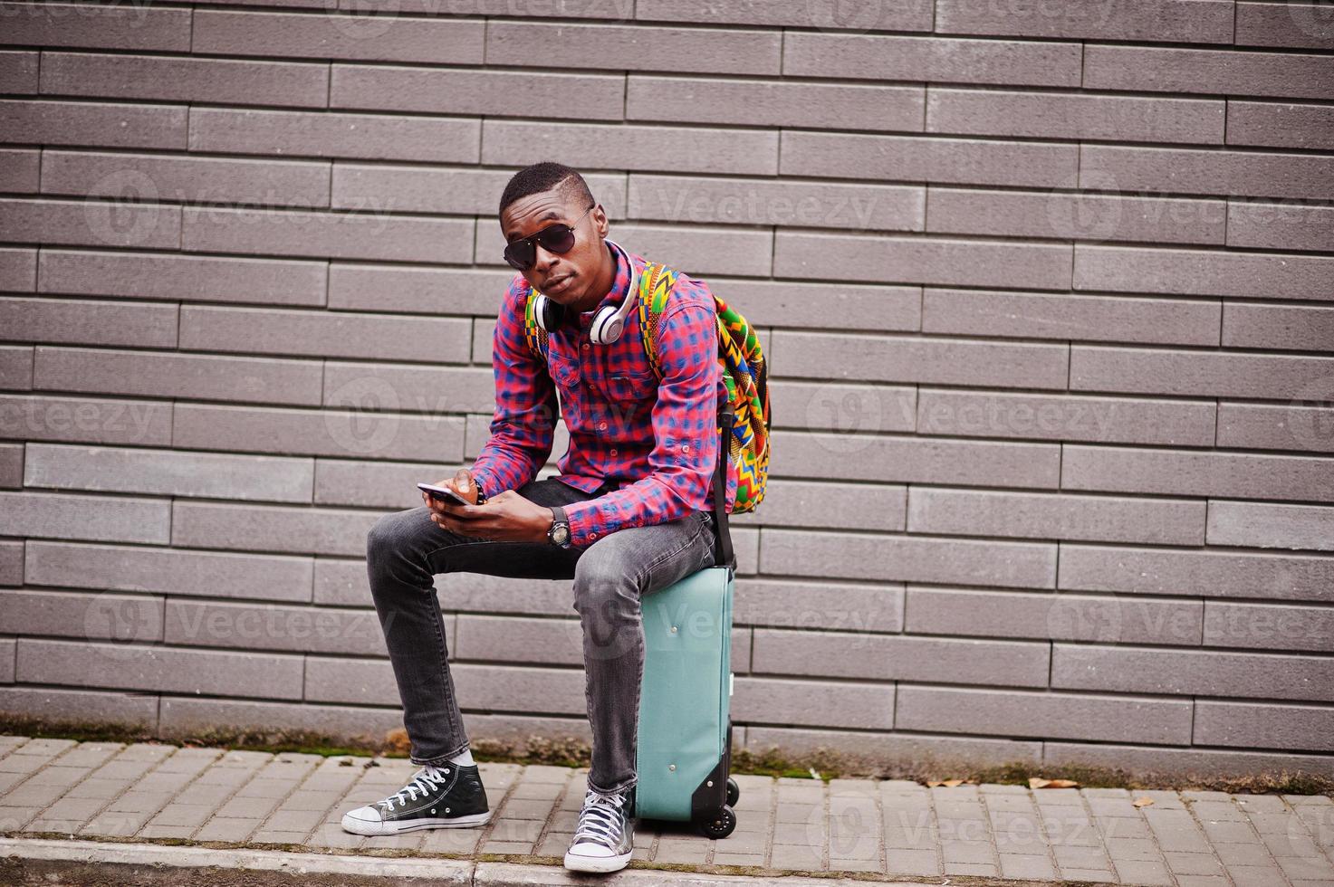 homme afro-américain en chemise à carreaux, avec valise et sac à dos.  voyageur d'homme noir au parc d'automne parlant au téléphone portable.  10570233 Photo de stock chez Vecteezy