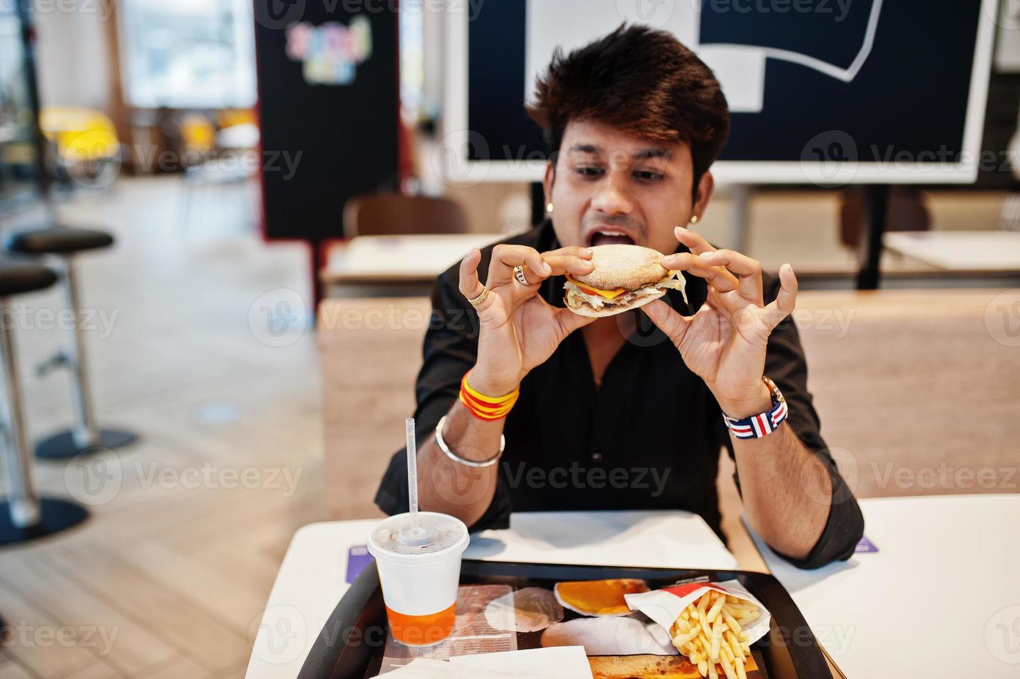 homme indien élégant assis au café de restauration rapide et manger un hamburger. photo