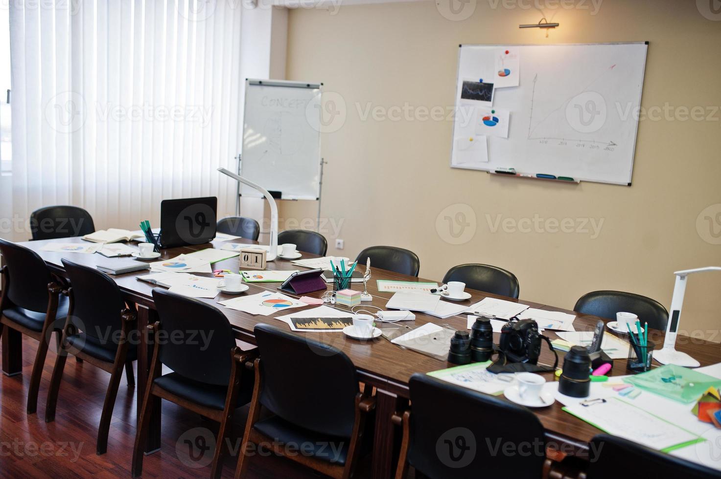 intérieur de bureau d'affaires moderne contenant des tables et des chaises, un ordinateur portable, un appareil photo et des fournitures de bureau sans employés.