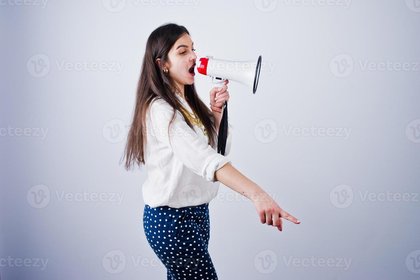 portrait d'une jeune femme en pantalon bleu et chemisier blanc posant avec mégaphone en studio. photo