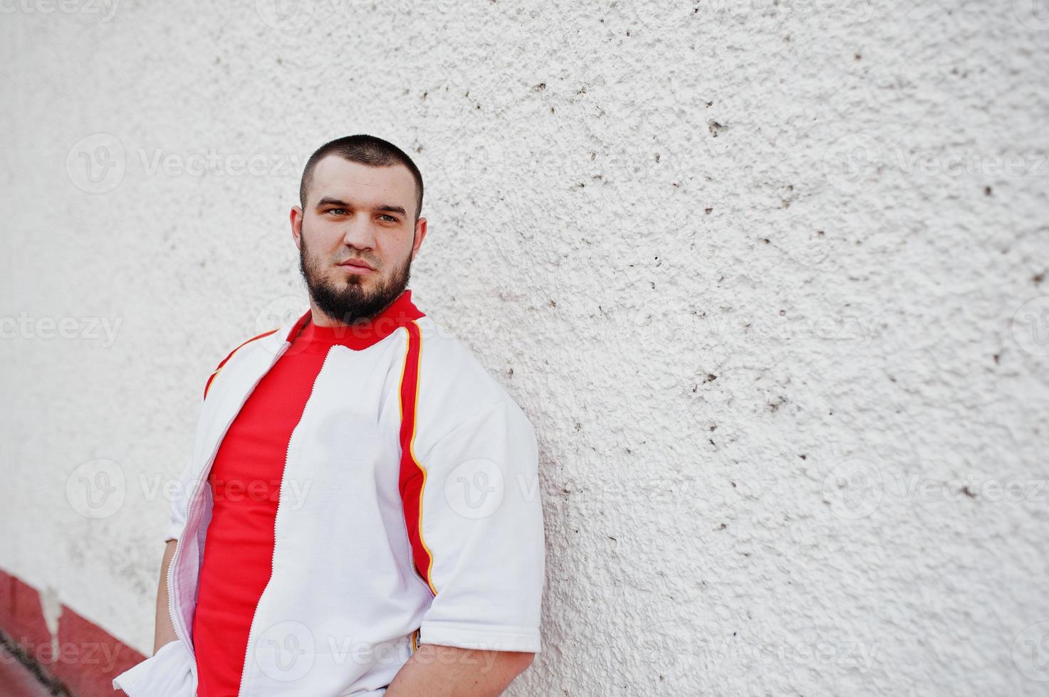 jeune homme musclé barbu brutal porte un costume de sport blanc avec une chemise rouge. photo