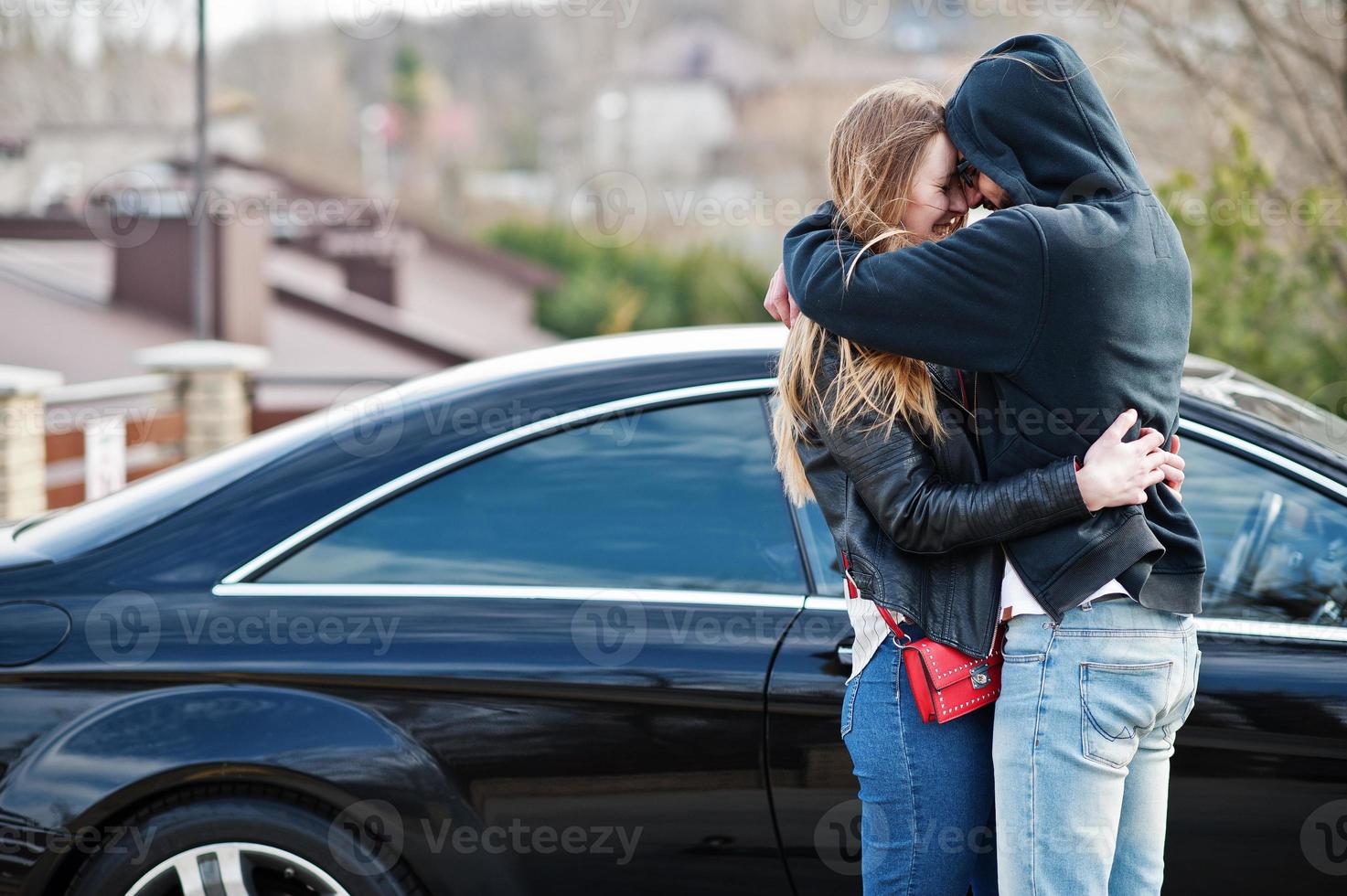 un couple multiracial cool se serre contre une élégante voiture de sport noire. photo