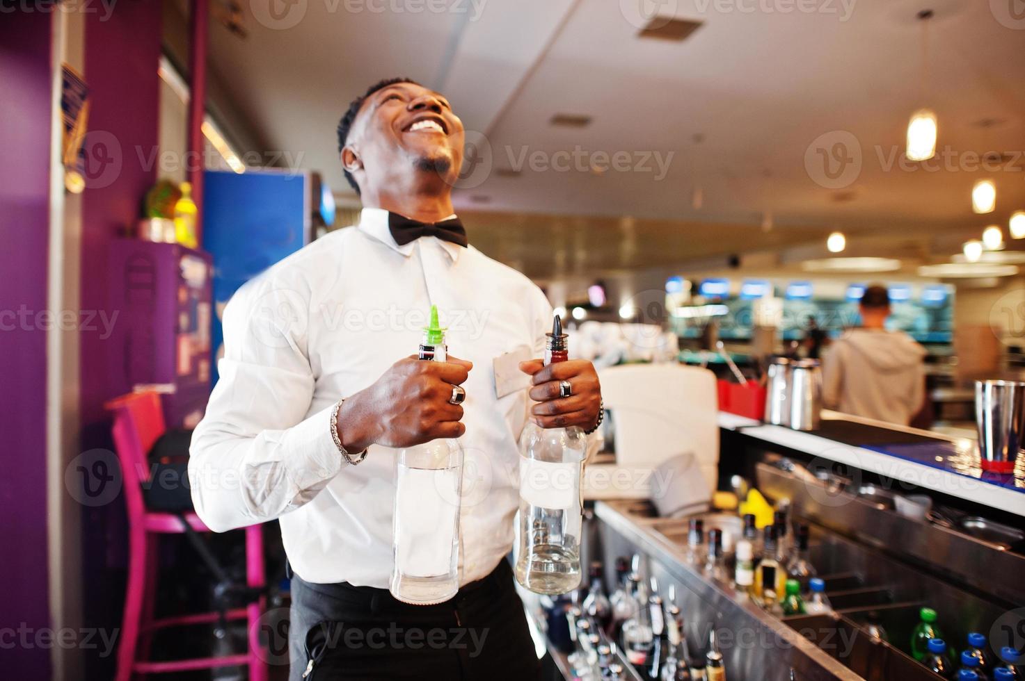 barman afro-américain au bar avec deux bouteilles. préparation de boissons alcoolisées. photo