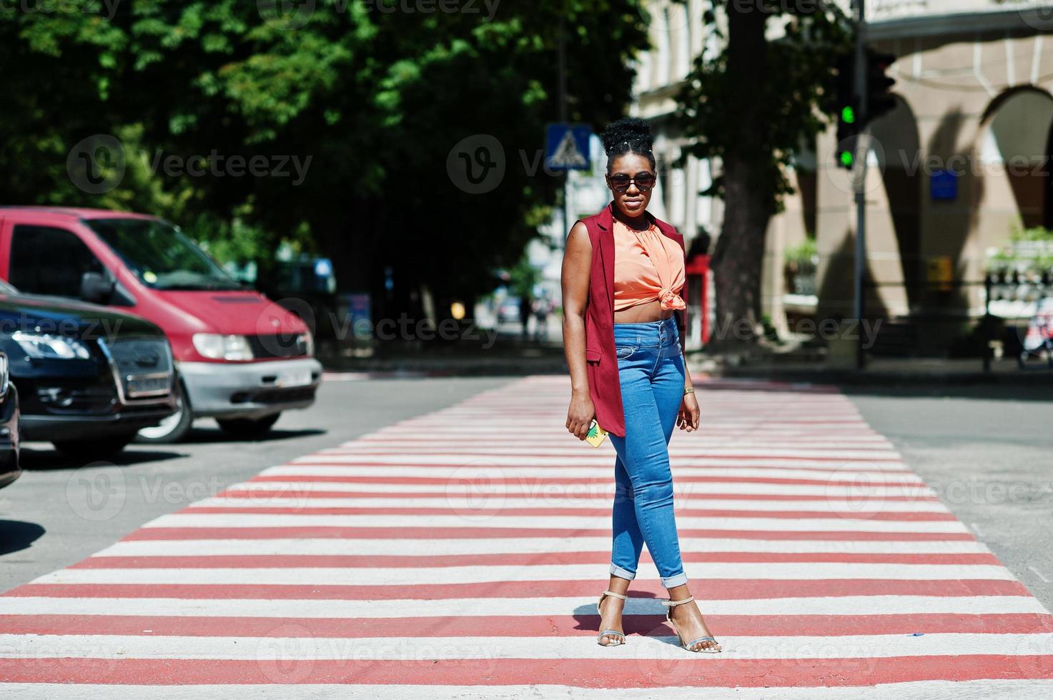 élégante femme afro-américaine marchant sur un passage pour piétons ou un passage pour piétons avec un téléphone portable à portée de main. photo