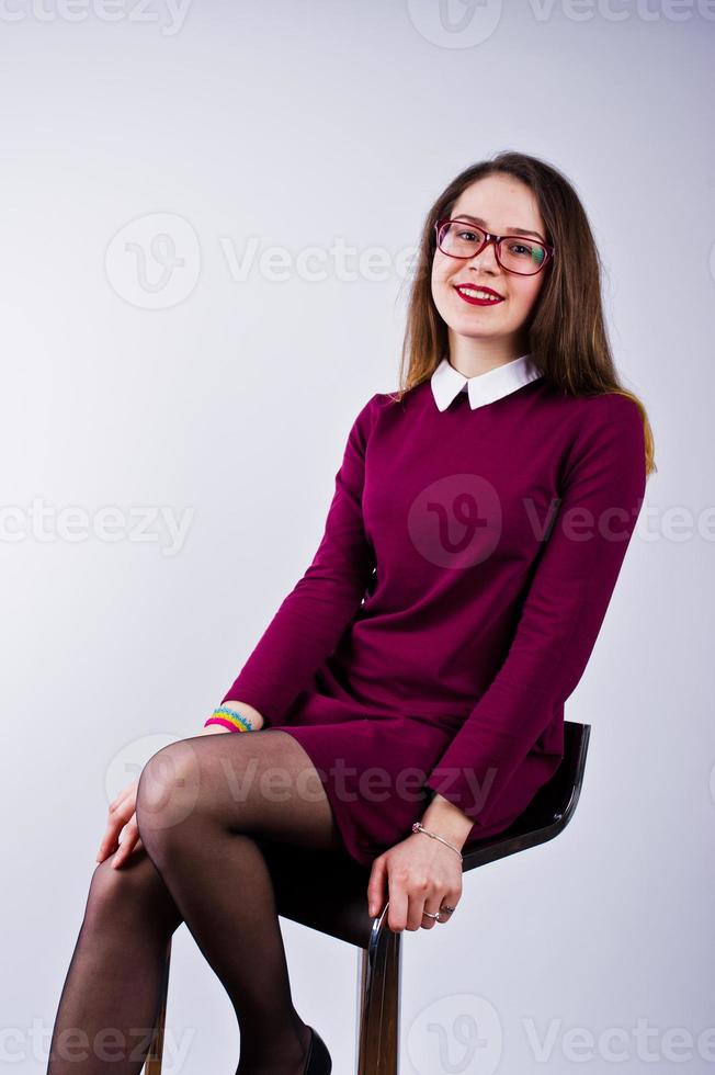 portrait d'une jeune femme en robe violette et lunettes assise sur la chaise dans le studio. photo