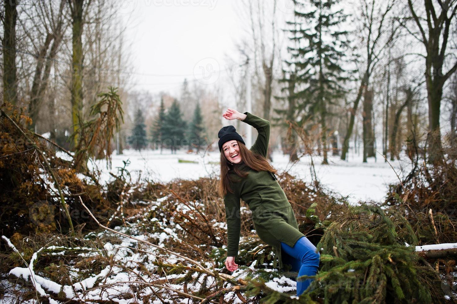 jeune fille porte un long sweat-shirt vert, un jean et un couvre-chef noir sur les branches du pin en journée d'hiver. photo