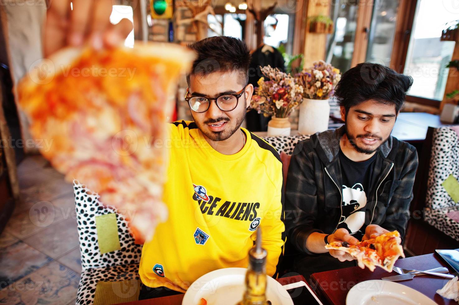 amis asiatiques gars mangeant de la pizza pendant la fête à la pizzeria. des indiens heureux s'amusant ensemble, mangeant de la nourriture italienne et assis sur un canapé. photo