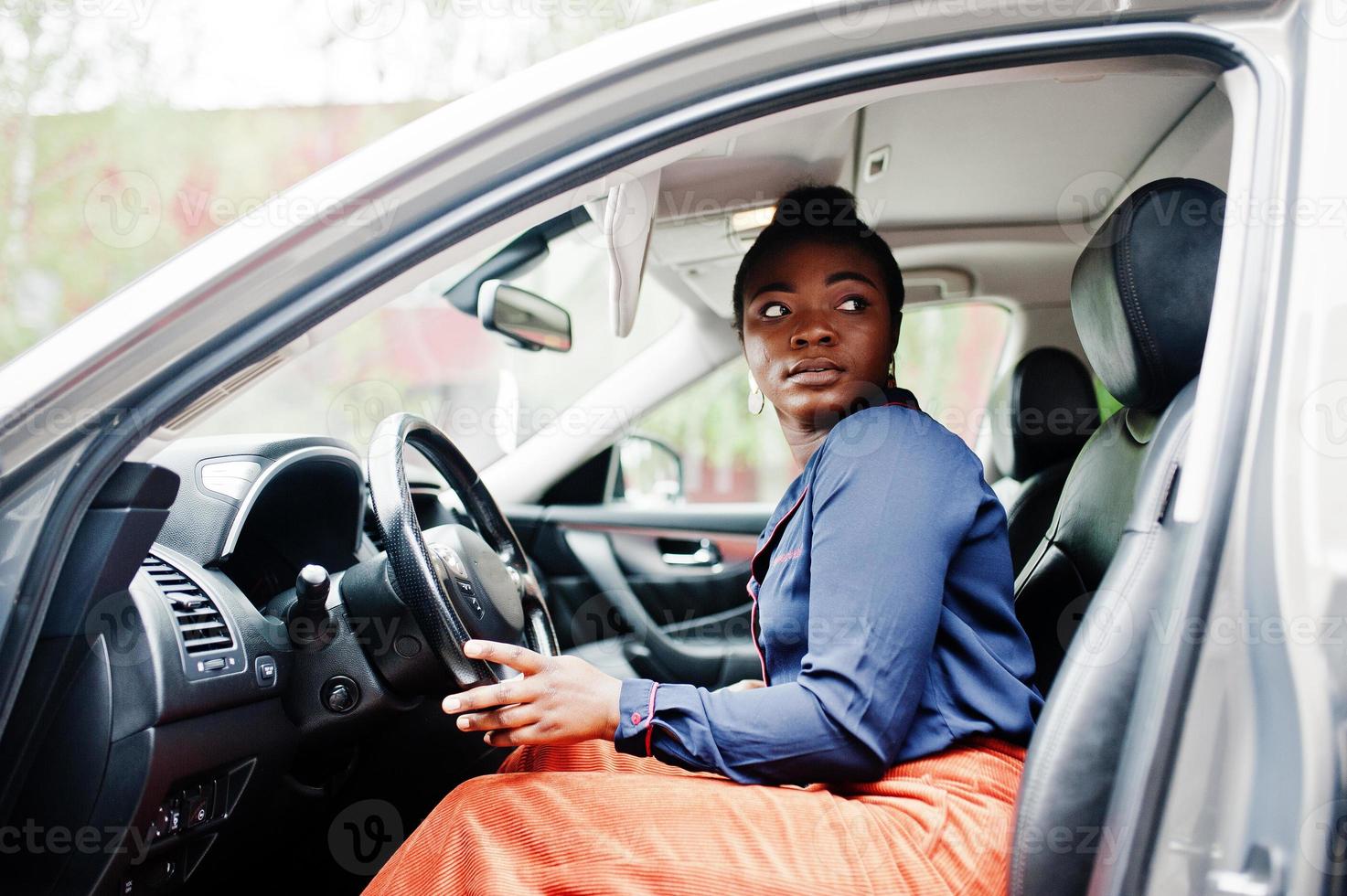 riche femme africaine d'affaires s'asseoir sur le siège du conducteur à la voiture suv argentée avec porte ouverte. photo