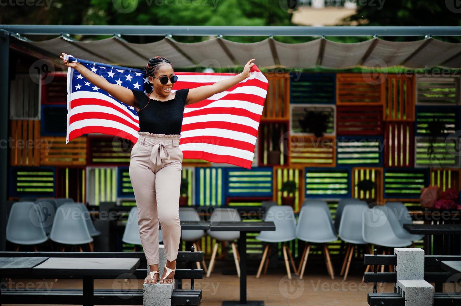 élégante femme afro-américaine à lunettes de soleil posée en plein air avec le drapeau américain. photo