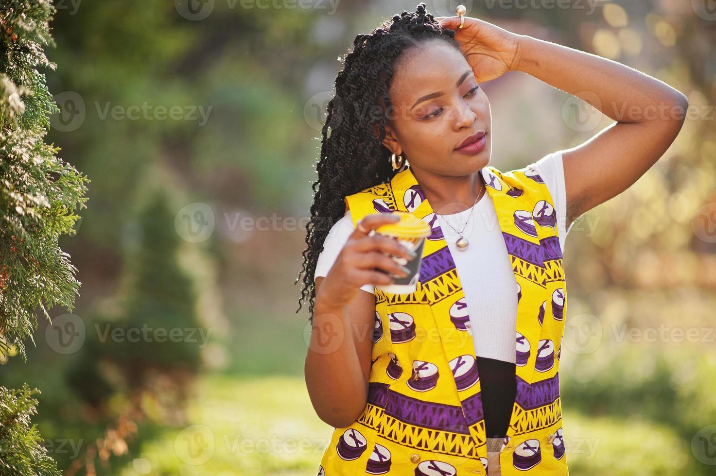 élégantes femmes afro-américaines en veste jaune posées dans la rue avec une boisson chaude dans une tasse en papier jetable. photo