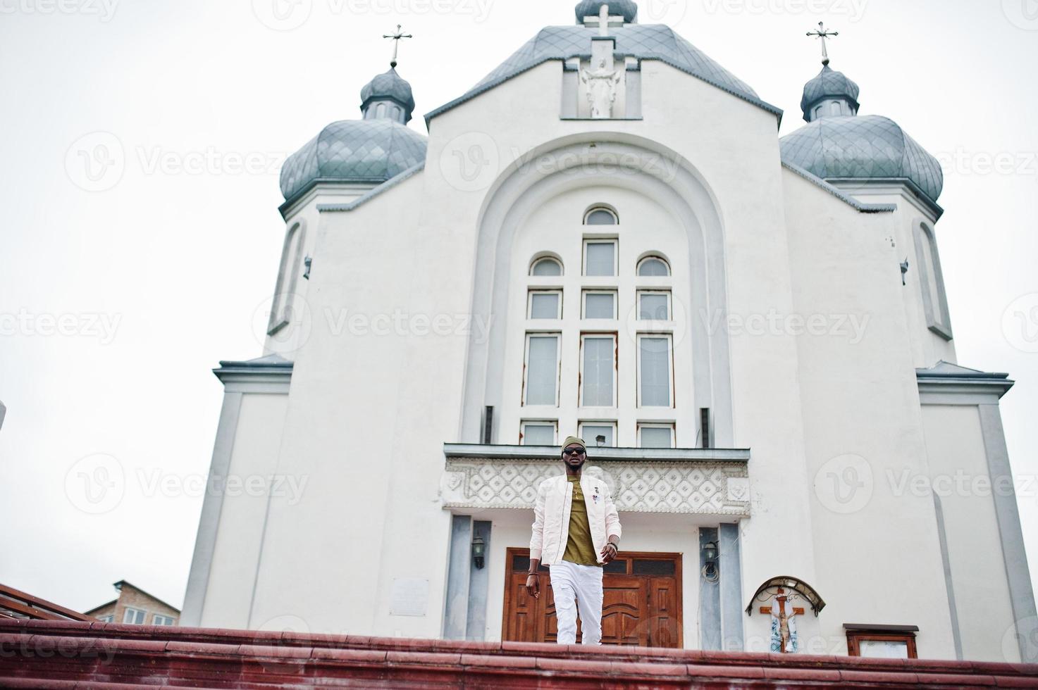 un homme afro-américain au chapeau et aux lunettes de soleil se tient contre l'église. Foi et christianisme en Afrique. photo