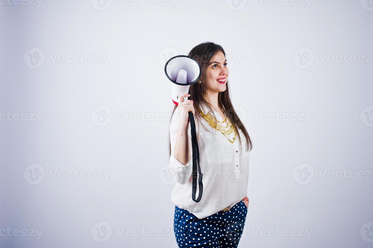 portrait d'une jeune femme en pantalon bleu et chemisier blanc posant avec mégaphone en studio. photo