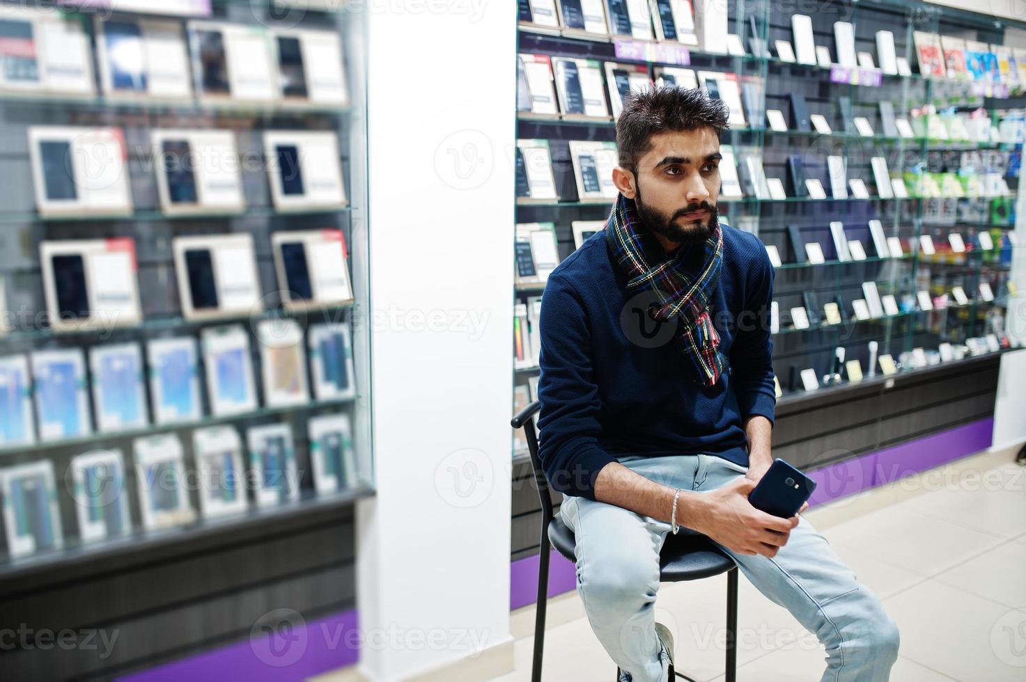 Acheteur client indien barbe homme au magasin de téléphonie mobile assis sur une chaise avec smartphone à portée de main. concept de peuples et de technologies d'asie du sud. magasin de téléphonie mobile. photo