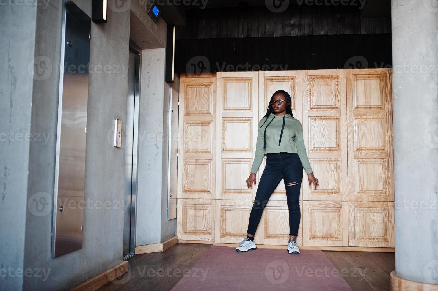 portrait de la ville d'une jeune femme positive à la peau foncée portant un sweat à capuche vert et des lunettes. photo