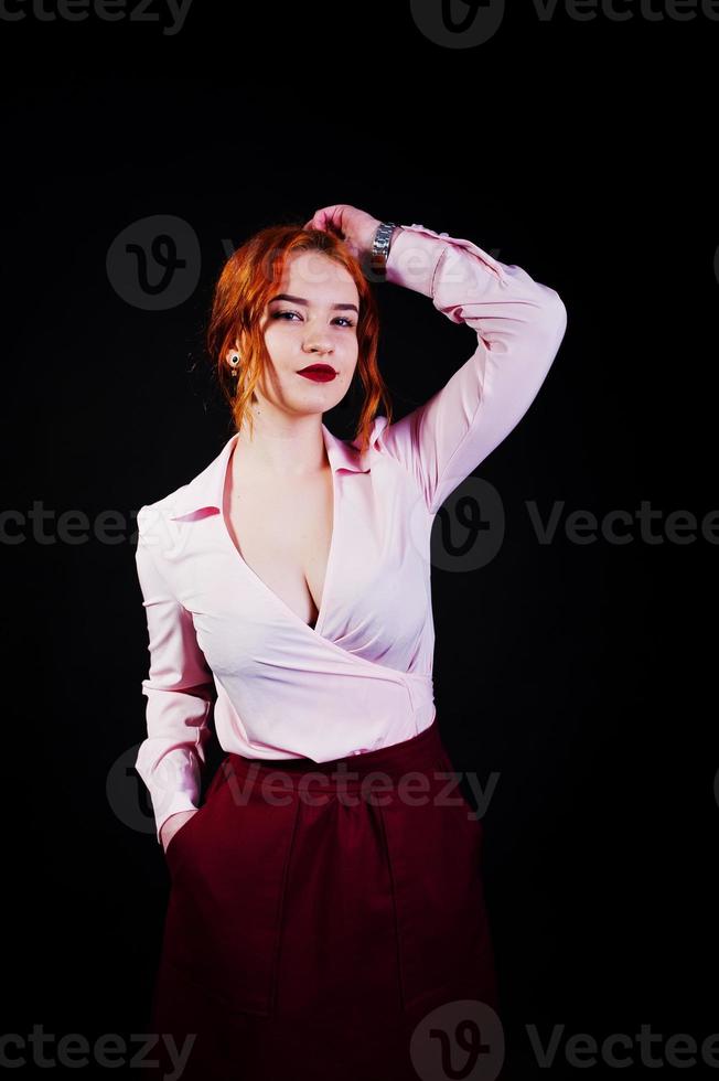 portrait d'une fille rousse en blouse rose et jupe marsala sur fond noir. photo