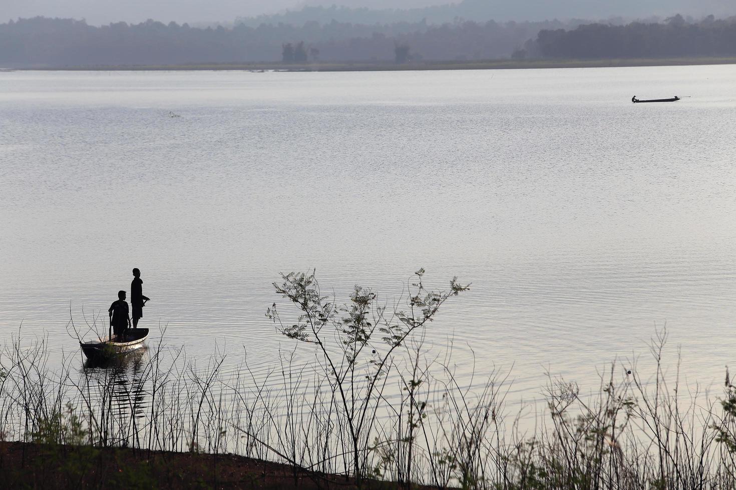 silhouette de pêcheur sur bateau en bois au lac. photo