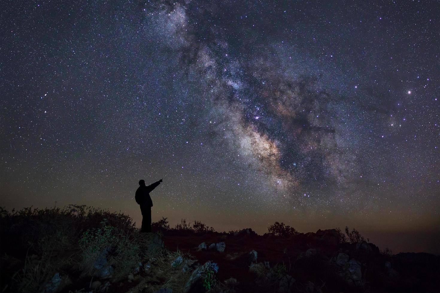 un homme se tient à côté de la galaxie de la voie lactée pointant sur une étoile brillante, une photographie à longue exposition, avec du grain photo