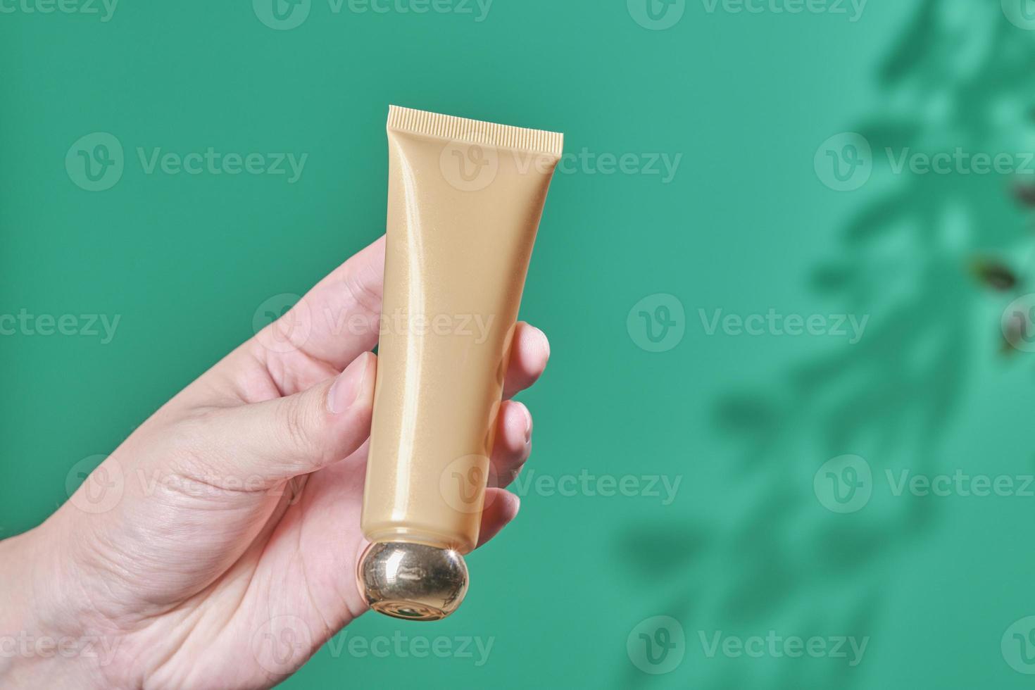 la main féminine tient un produit cosmétique dans un tube, une bouteille en verre, une lotion, une crème hydratante anti-âge, une huile essentielle pour le visage ou un sérum sur fond vert avec une nature d'ombre légère. concept de soins cosmétiques de beauté. photo