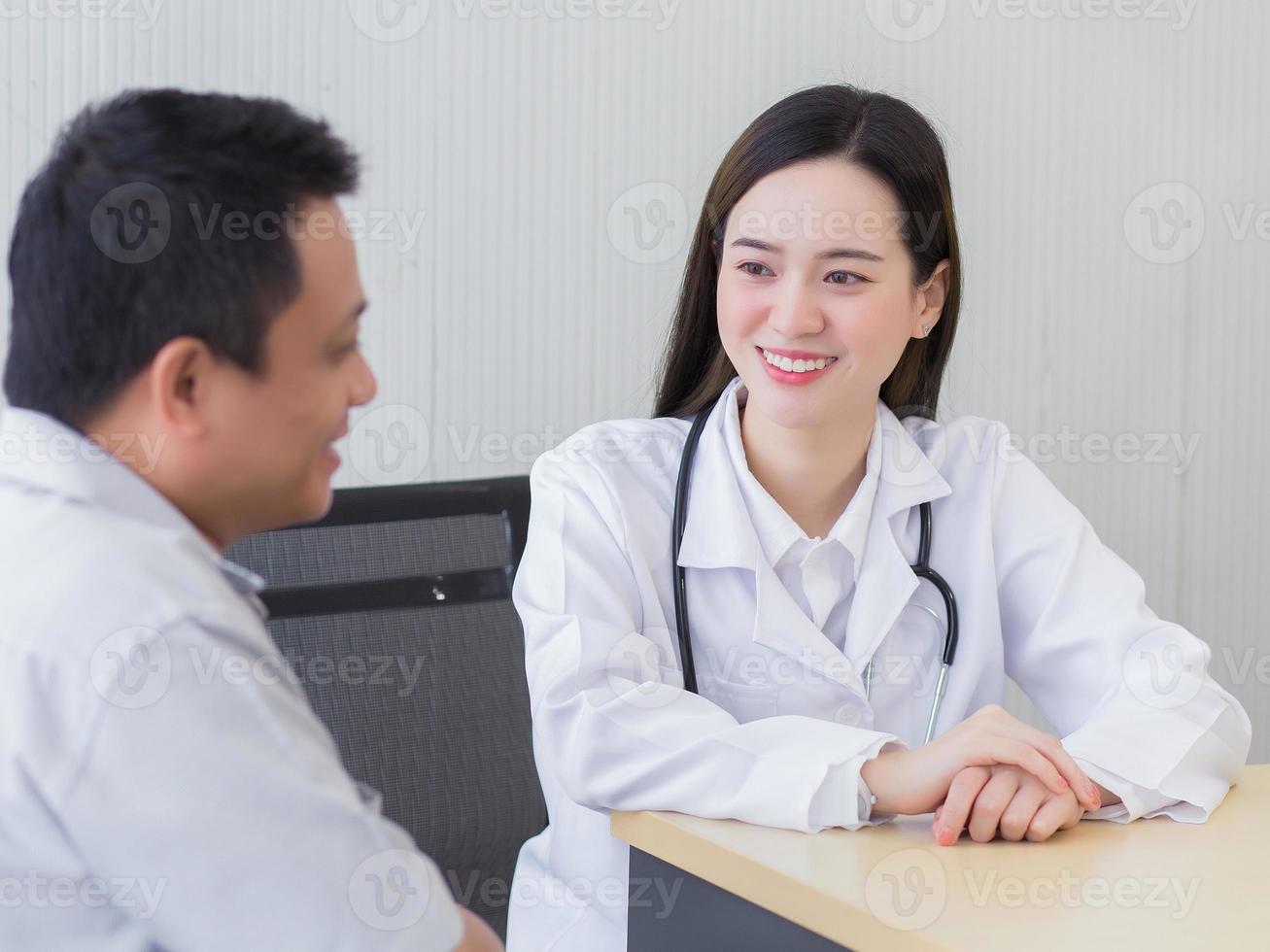 belle jeune femme médecin asiatique professionnelle parlant avec un homme patient de sa douleur et de ses symptômes pendant qu'ils mettent un masque facial et un thermomètre sur la table dans la salle d'examen photo