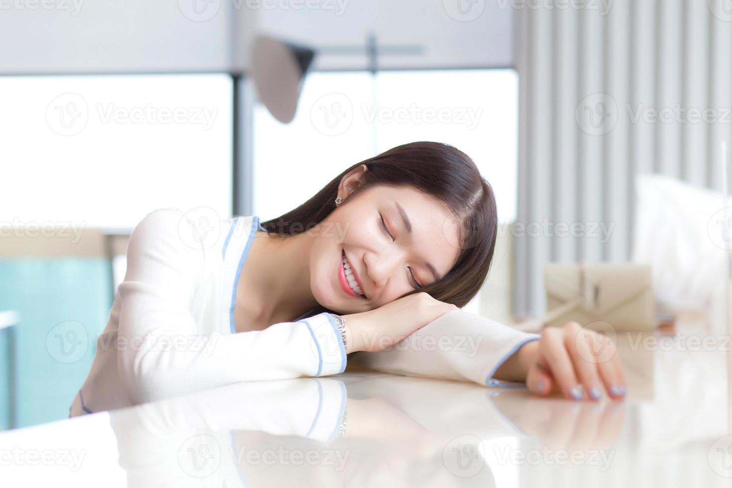 portrait d'une belle jeune femme est assise les yeux fermés joyeusement sur le bureau. modèle femme s'asseoir dans la salle vitrée. photo