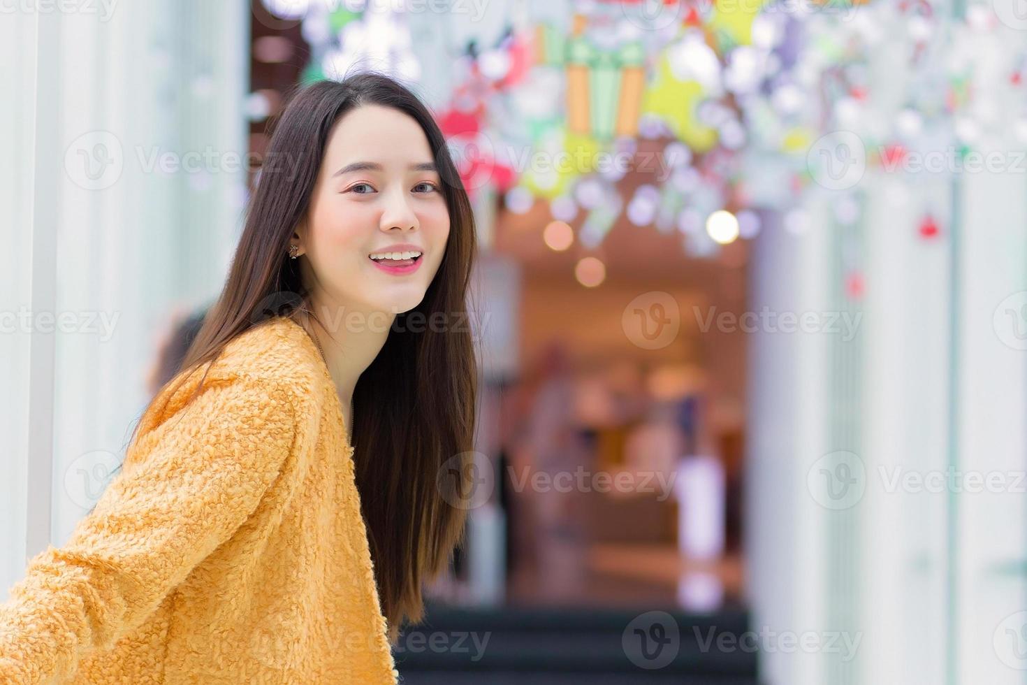 belle femme asiatique aux cheveux longs porte un manteau jaune et sourit joyeusement. dans le thème pour fêter noël et bonne année photo