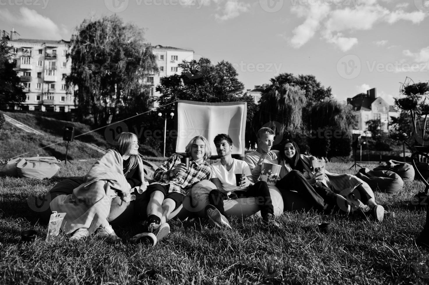 jeune groupe multiethnique de personnes regardant un film au pouf dans un cinéma en plein air. photo