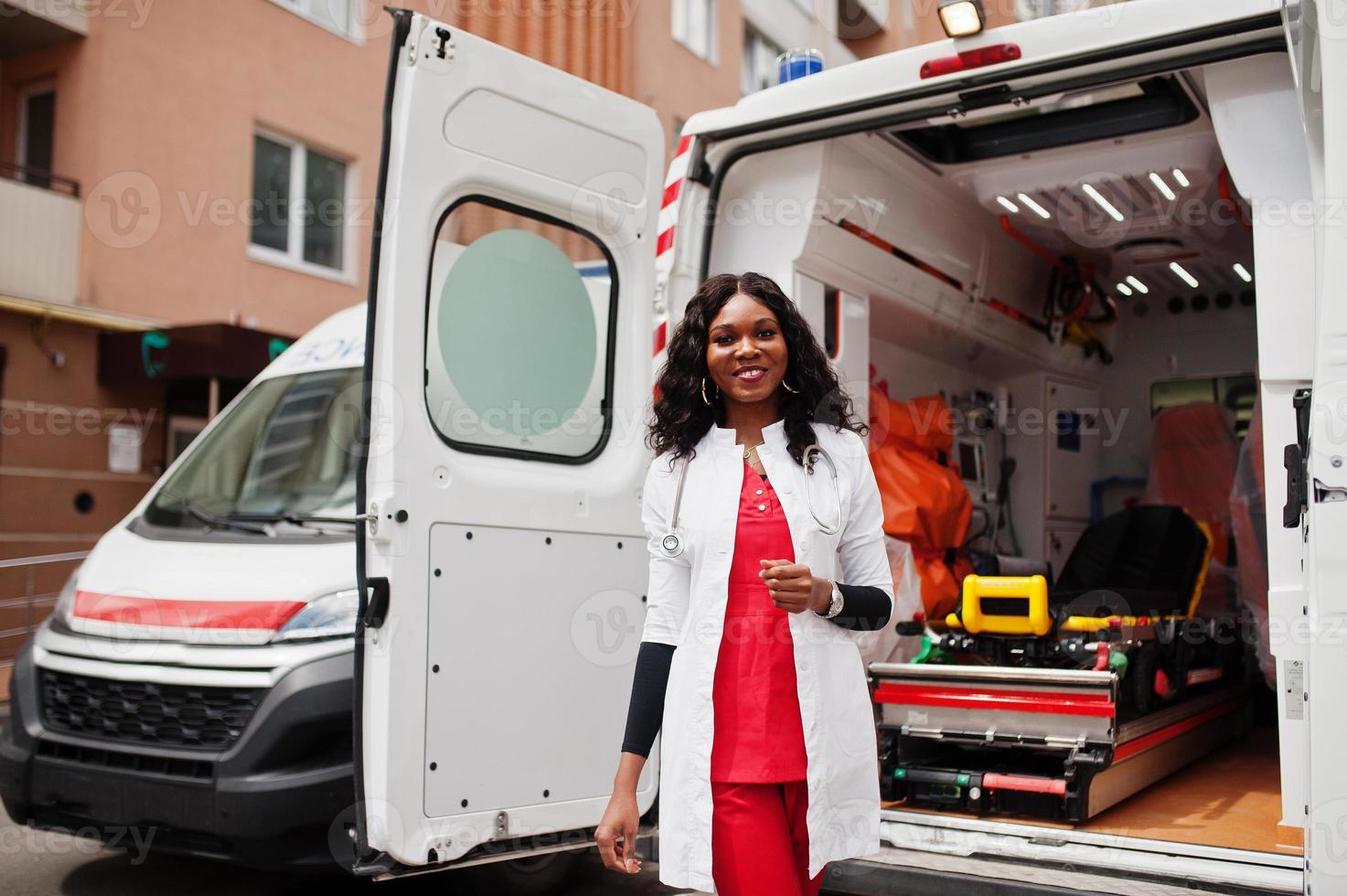 paramédic femme afro-américaine debout devant la voiture d'ambulance. photo