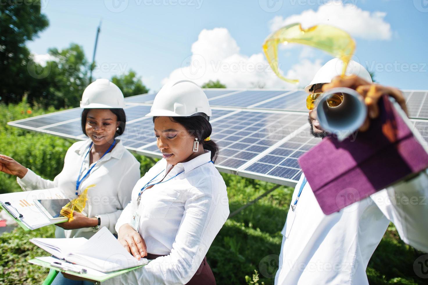 un technicien afro-américain vérifie l'entretien des panneaux solaires. groupe de trois ingénieurs noirs réunis à la station solaire. photo