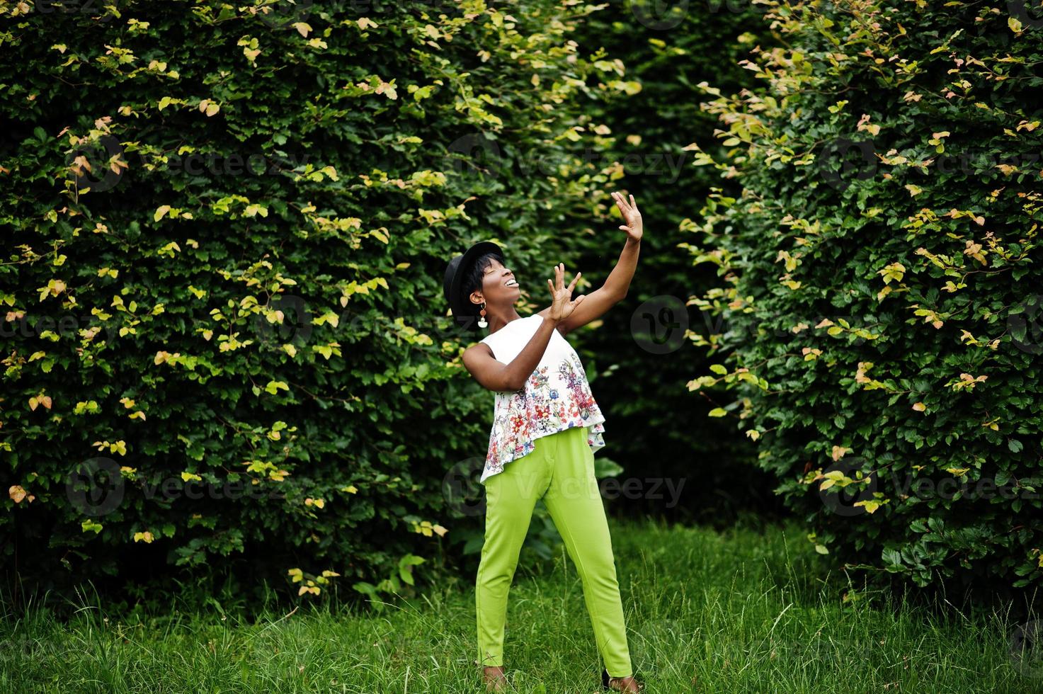 incroyable femme modèle afro-américaine en pantalon vert et chapeau noir posé au parc. photo