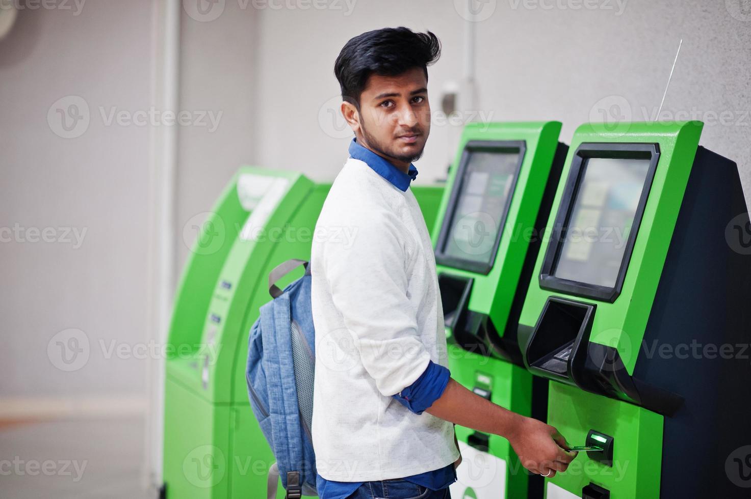 un jeune homme asiatique a mis sa carte de crédit pour retirer de l'argent d'un guichet automatique vert. photo