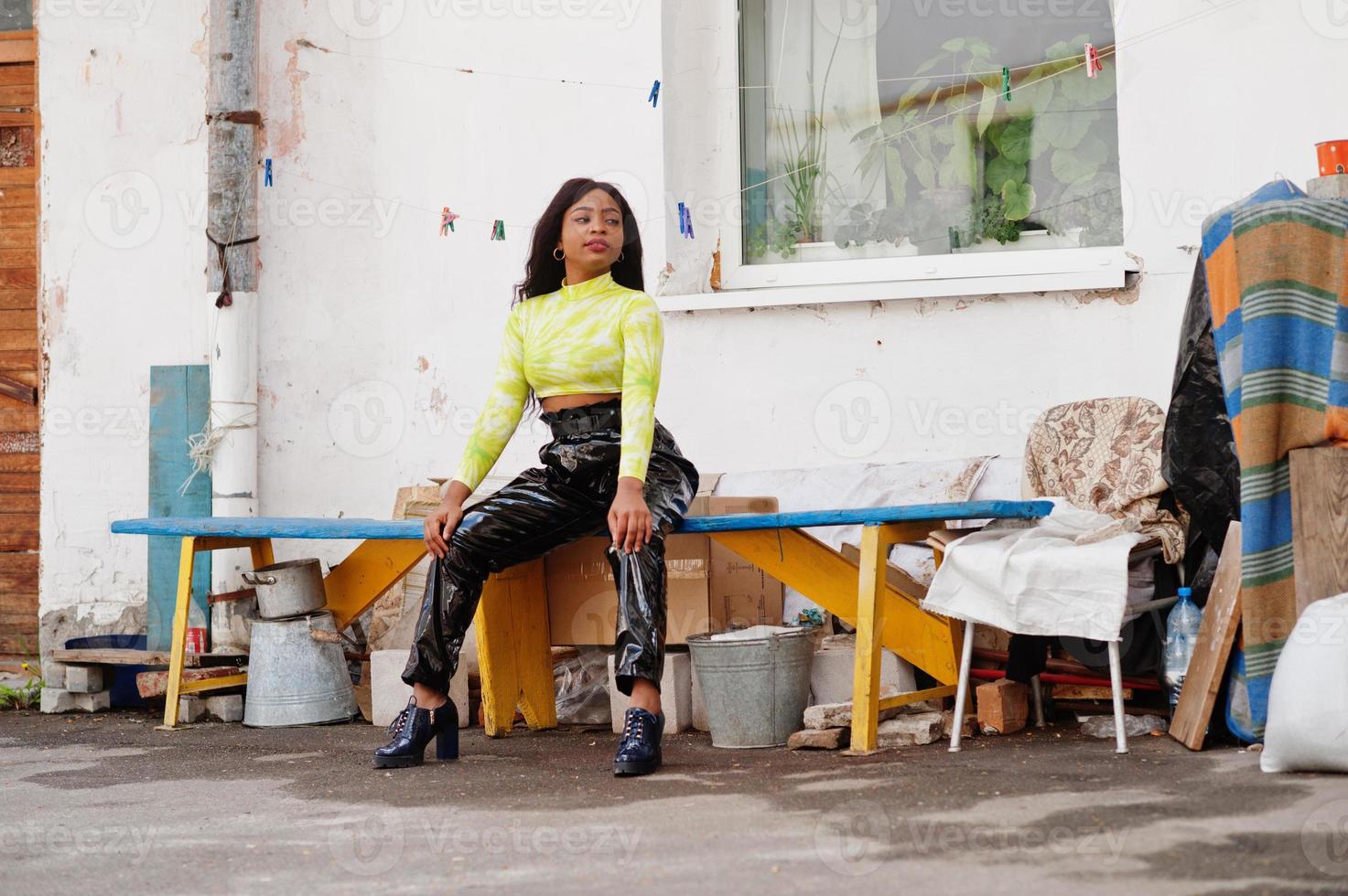 portrait d'une belle jeune femme mannequin afro-américaine, vêtue d'un haut vert et d'un pantalon noir brillant à l'aspect mouillé. photo