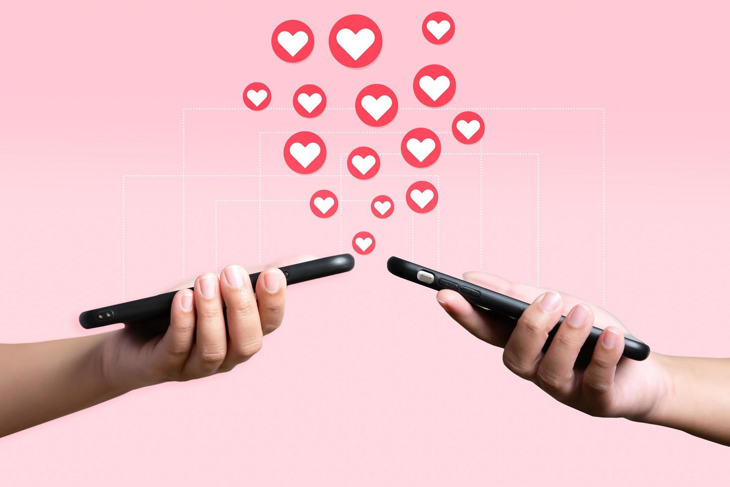 les gens utilisent un téléphone portable pour s'envoyer du cœur. concept d'amour et de connexion à l'aide d'une application téléphonique sur fond rose. photo