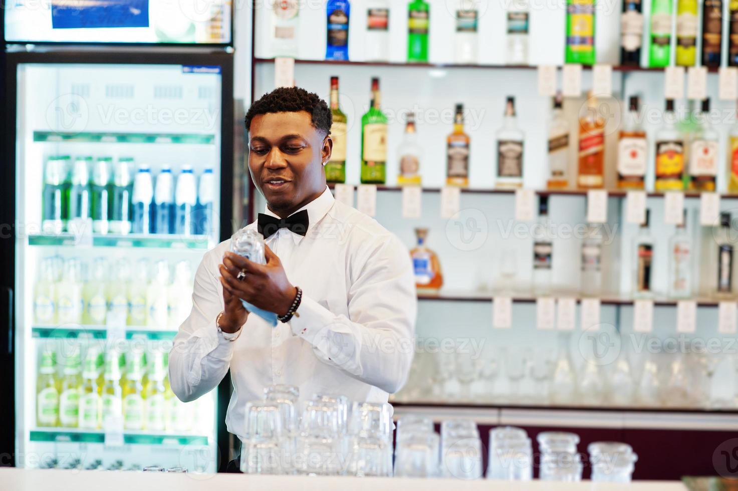 le barman afro-américain porte des lunettes de nettoyage à nœud papillon au bar. photo