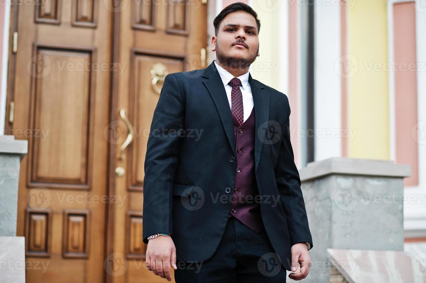 homme d'affaires indien élégant en tenue de soirée debout contre la porte du centre d'affaires. photo