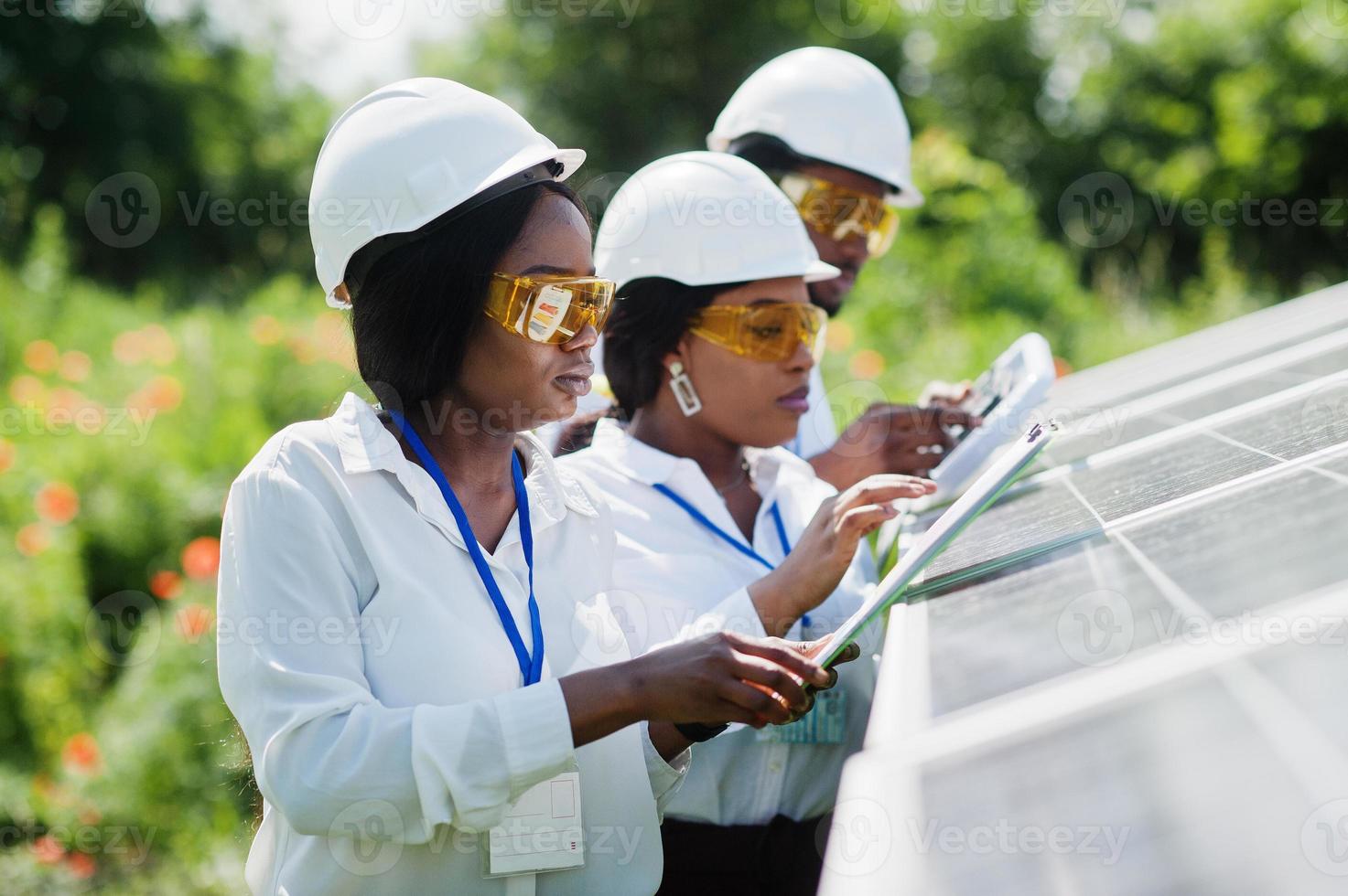 un technicien afro-américain vérifie l'entretien des panneaux solaires. groupe de trois ingénieurs noirs réunis à la station solaire. photo