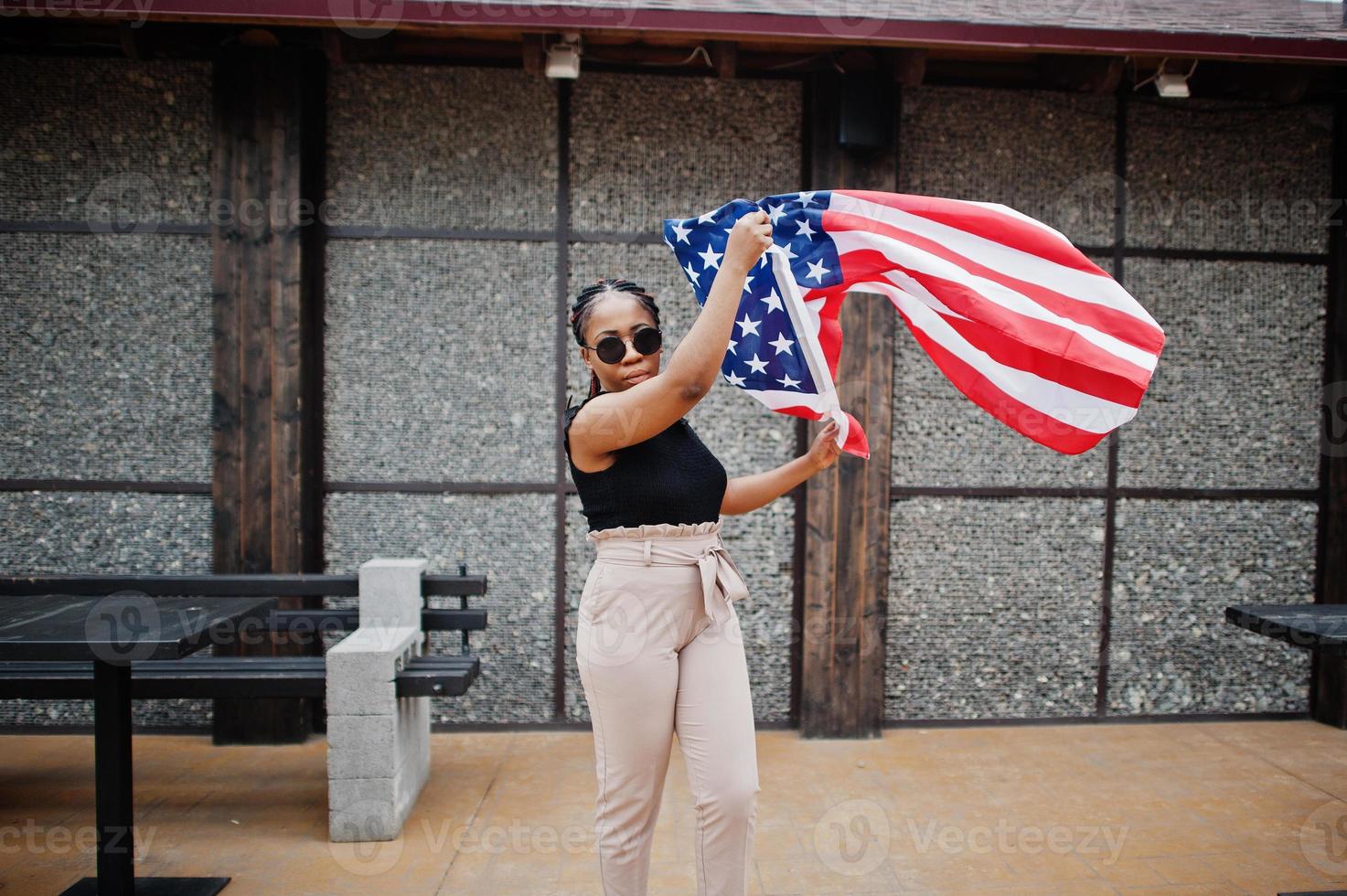 élégante femme afro-américaine à lunettes de soleil posée en plein air avec le drapeau américain. photo