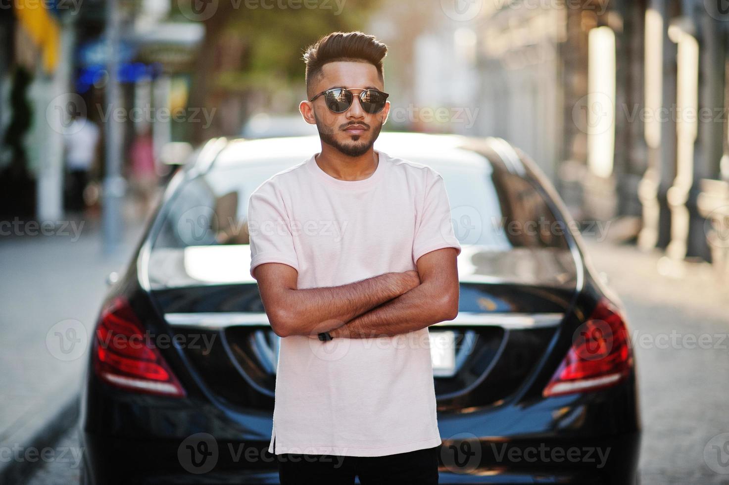 homme de barbe indien élégant à lunettes de soleil et t-shirt rose contre voiture de luxe. modèle riche de l'inde posé en plein air dans les rues de la ville. photo