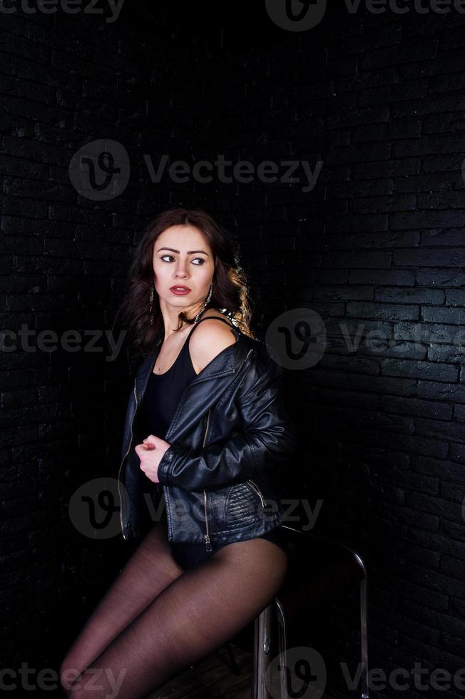 portrait en studio de fille brune sexy en veste de cuir noir contre le mur de briques. photo