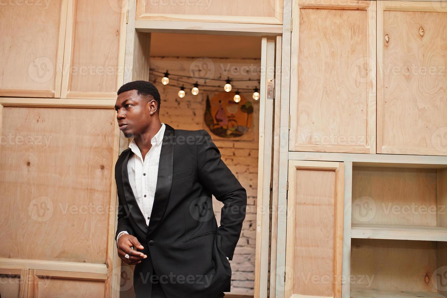 homme afro-américain puissant et fort en costume noir posant contre une bibliothèque en bois. photo