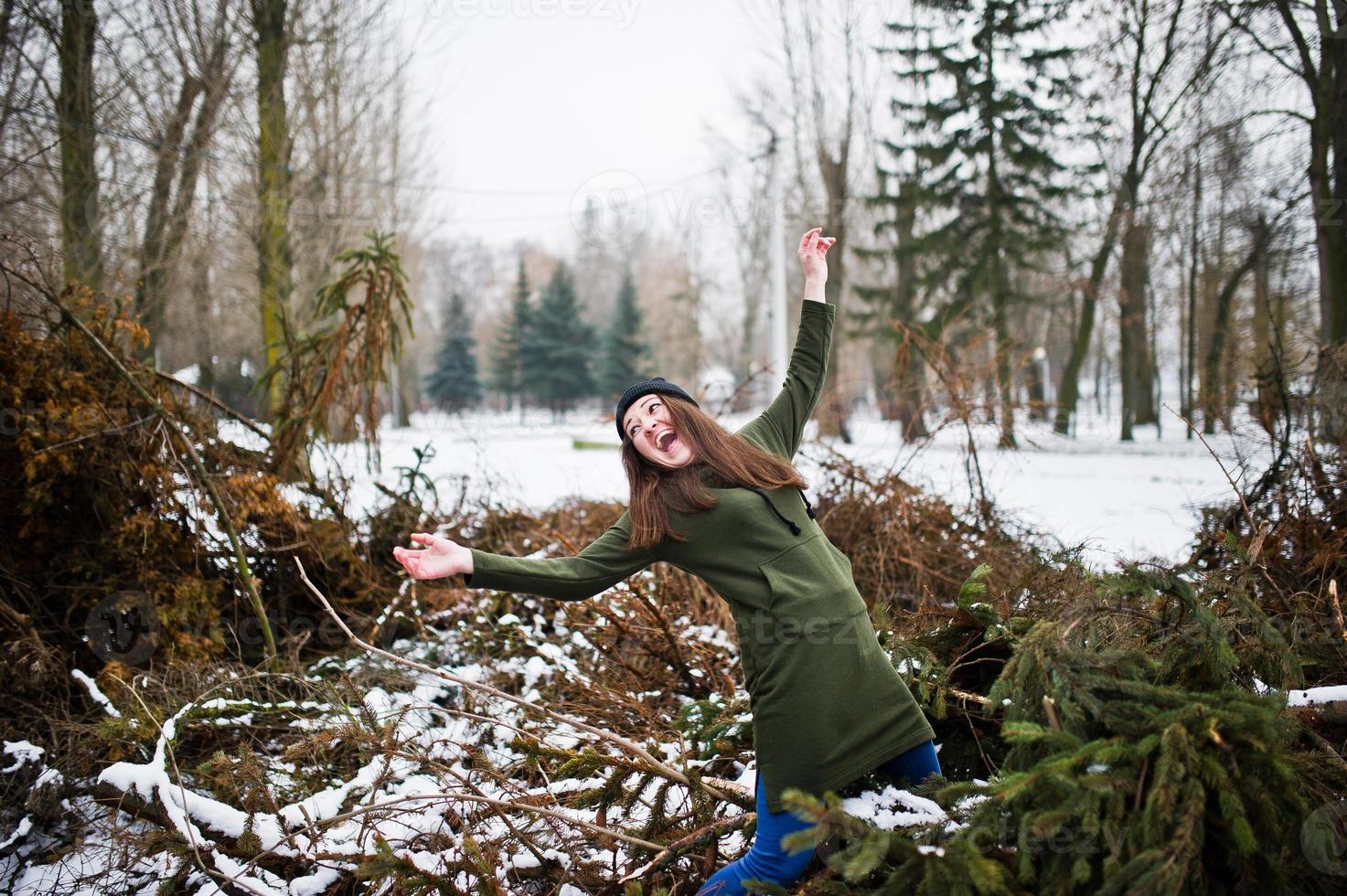 jeune fille porte un long sweat-shirt vert, un jean et un couvre-chef noir sur les branches du pin en journée d'hiver. photo