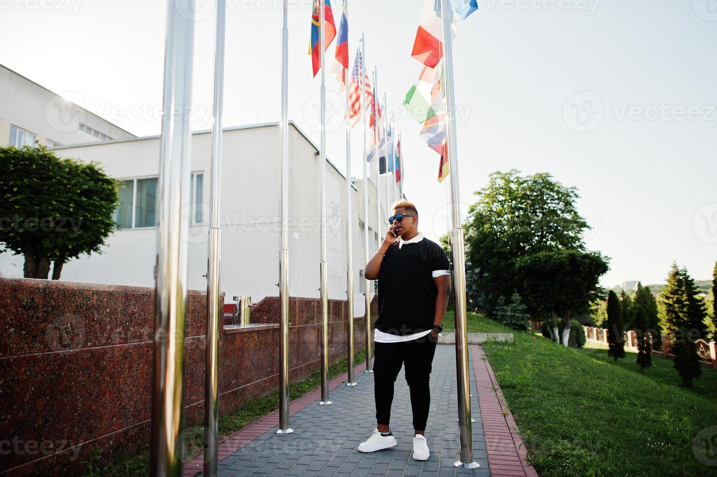 garçon musulman arabe élégant avec des cheveux à l'origine posés dans les rues, contre des drapeaux de différents pays. photo