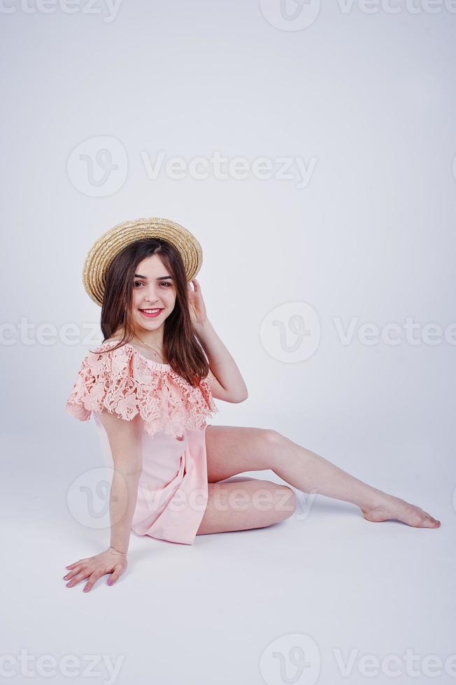 portrait d'une femme à la mode en robe rose assise et posant avec un chapeau sur le sol dans le studio. photo