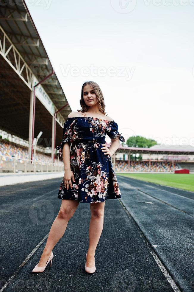 portrait d'une fille fabuleuse en robe et talons hauts sur la piste du stade. photo