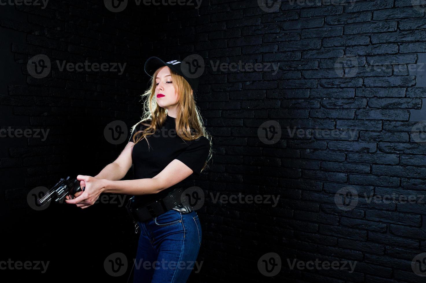 agent féminin du fbi en casquette et avec arme à feu au studio contre un mur de briques sombres. photo