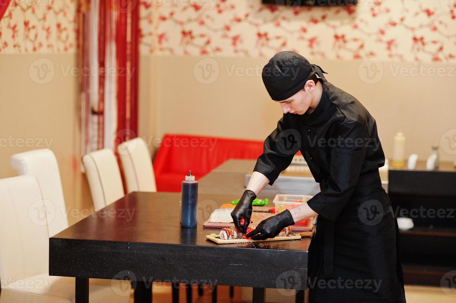 chef professionnel porter en noir faisant des sushis et des petits pains dans une cuisine de restaurant de cuisine traditionnelle japonaise. photo