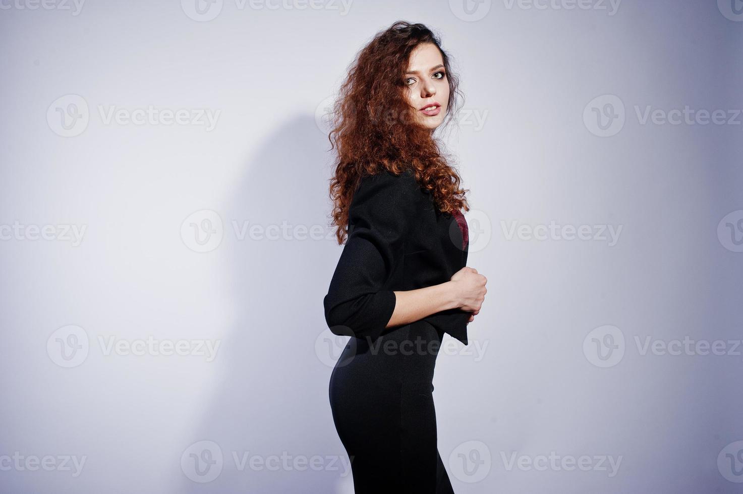 fille brune aux cheveux bouclés en veste de bureau noire avec jupe, sur soutien-gorge au studio sur fond blanc. femme d'affaires sexy. photo