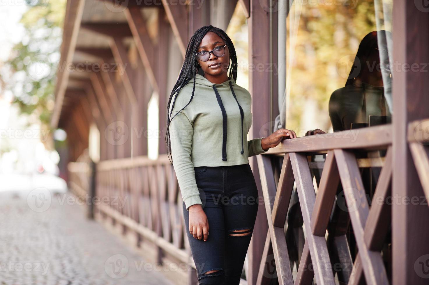 portrait de la ville d'une jeune femme positive à la peau foncée portant un sweat à capuche vert et des lunettes. photo