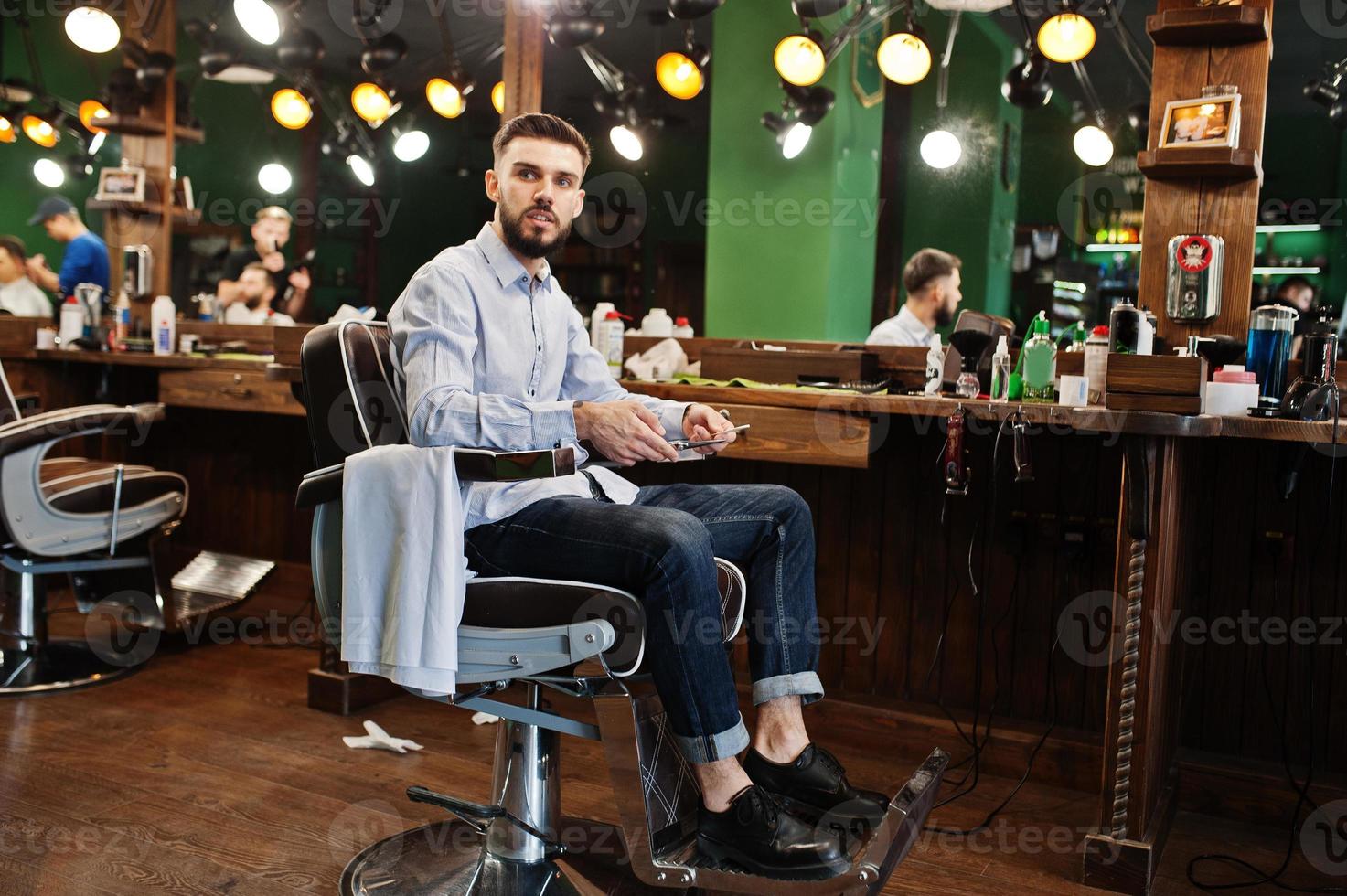 barbier beau barbu assis sur une chaise au salon de coiffure. photo